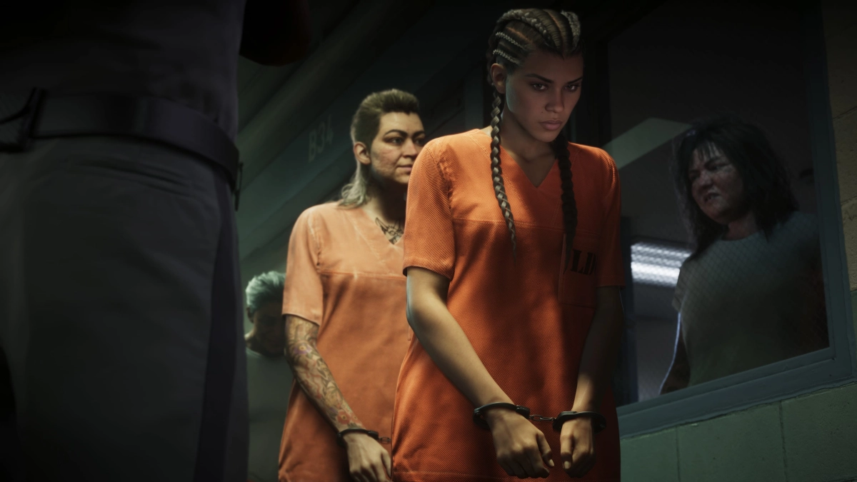 Inside a jail, Lucia and another woman are handcuffed and wearing orange jumpsuits as they walk by a window where another woman watches through the glass. An officer stands nearby.